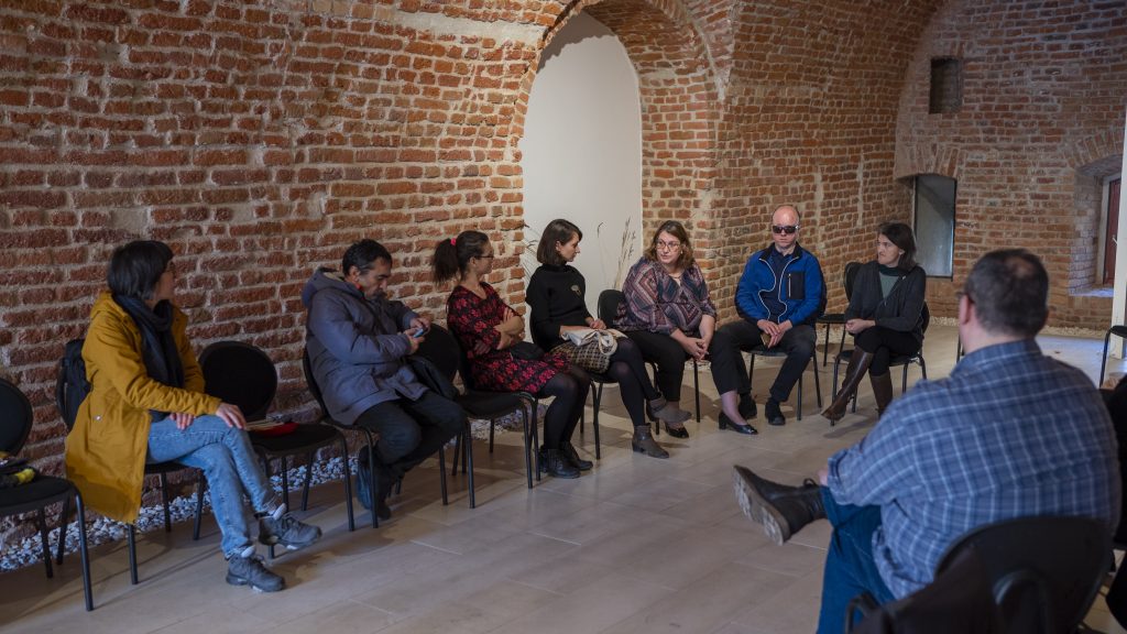 În această imagine se regăsesc mai multe persoane de gen feminin care stau pe scaune și povestesc
