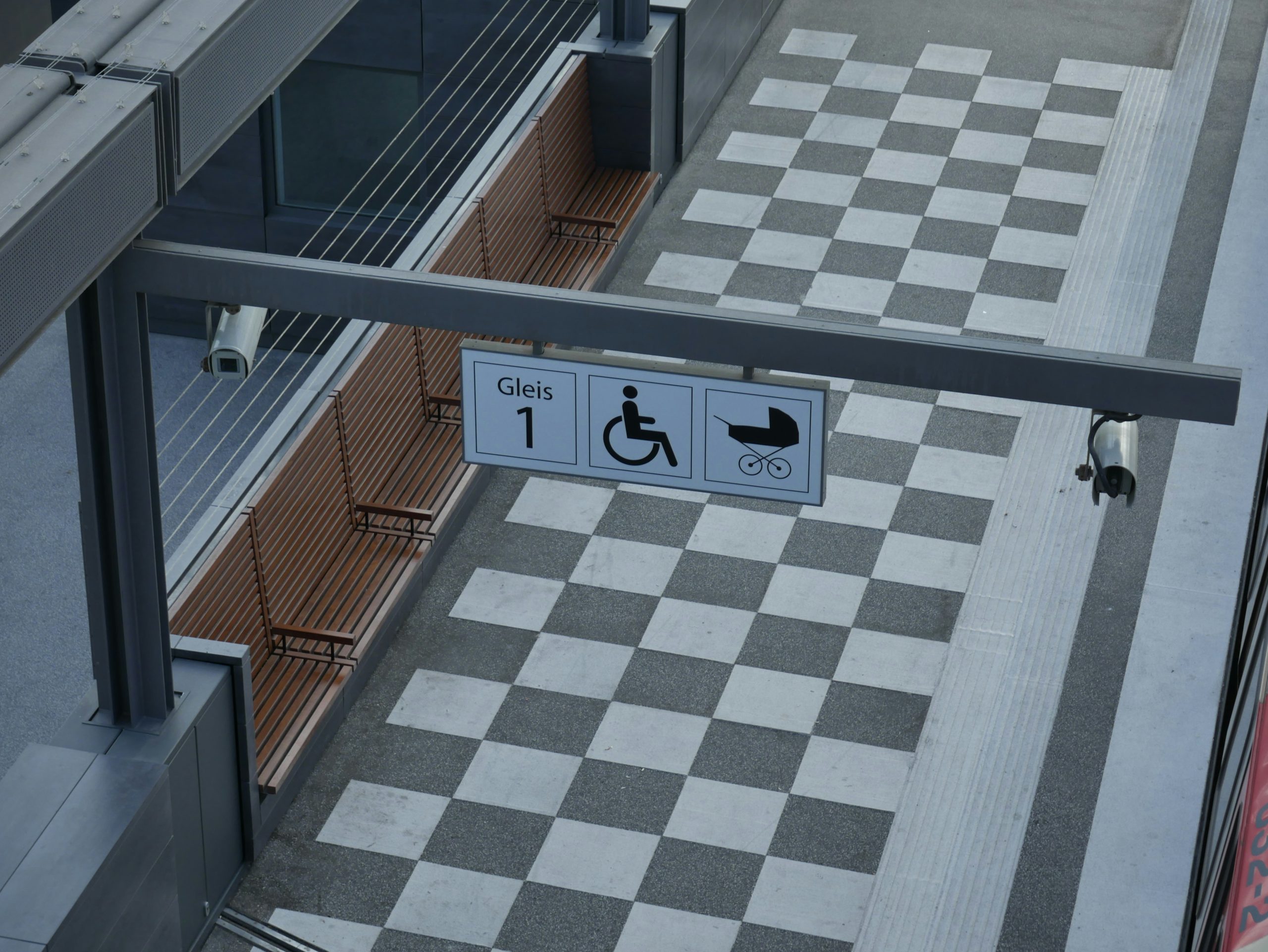 imaginea reprezinta o sala de asteptare la metrou, iar în partea de sus pe o bară metalică există 3 semne, respectiv peronul 1, semnul persoanelor cu dizabilități și un cărucior de copii.