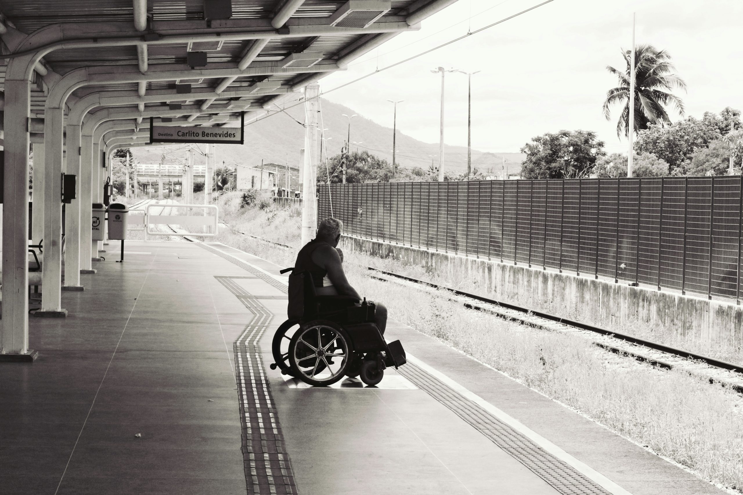 in imagine este un bărbat în scaun cu rotile care așteaptă pe peron un mijloc de transport în comun